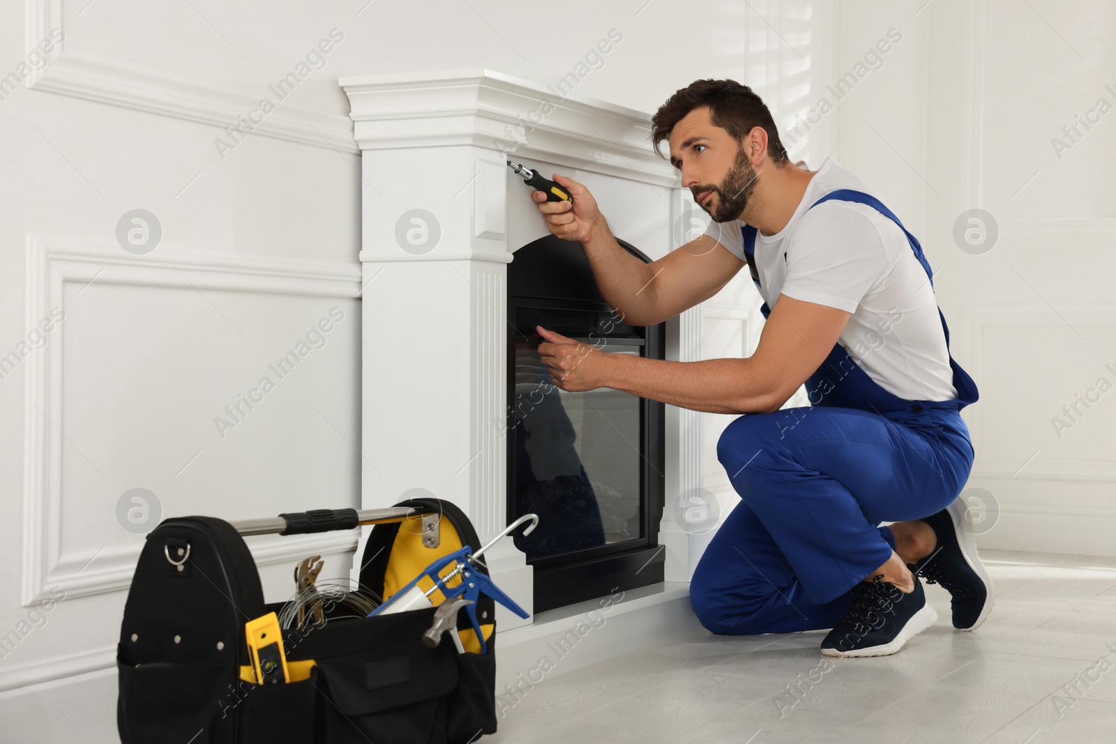 Photo of Professional technician with screwdriver installing electric fireplace in room