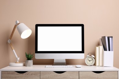 Cozy workspace with computer, lamp, houseplant and stationery on wooden desk