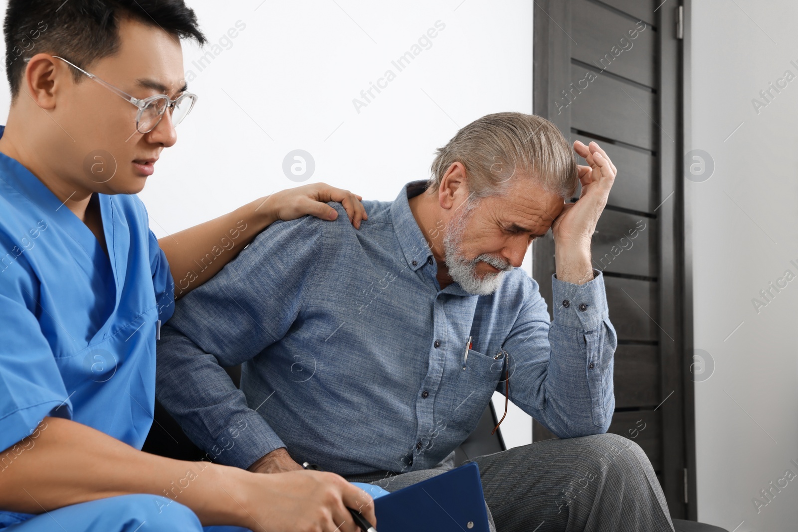 Photo of Doctor with clipboard consulting senior patient in clinic