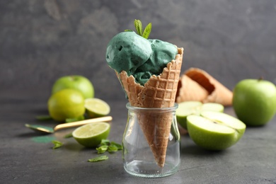 Composition with delicious spirulina ice cream cone on table against grey background