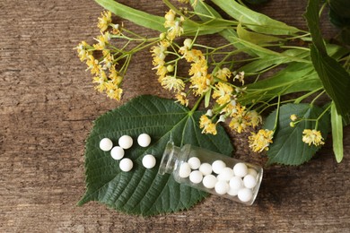 Photo of Bottle of homeopathic remedy, linden flowers and leaves on wooden background, flat lay