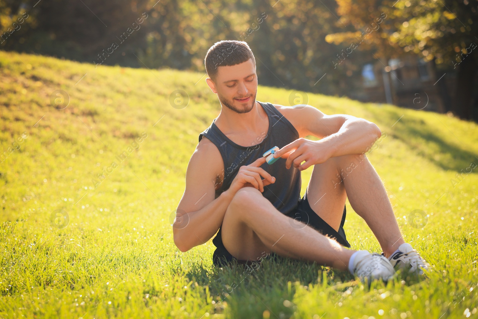 Photo of Happy man checking pulse with blood pressure monitor on finger after training in park. Space for text