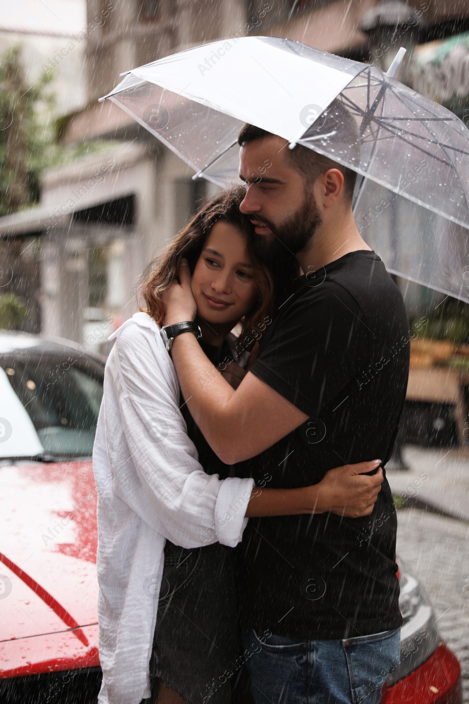 Photo of Young couple with umbrella enjoying time together under rain on city street