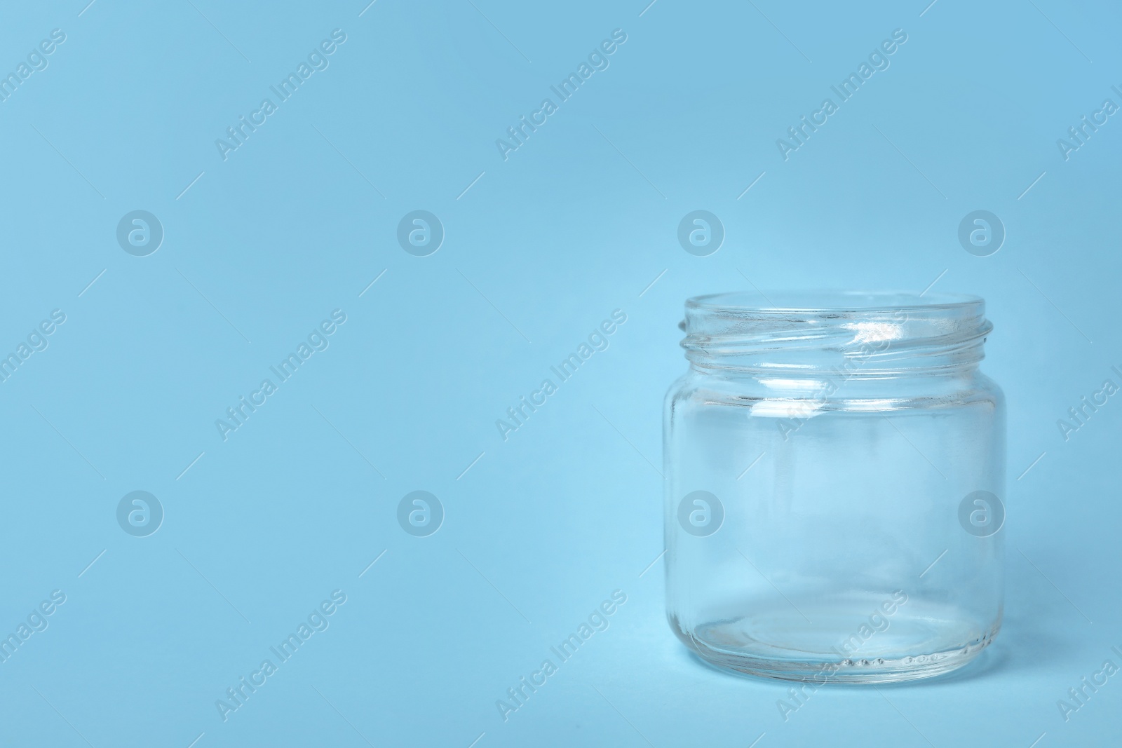 Photo of Open empty glass jar on light blue background, space for text