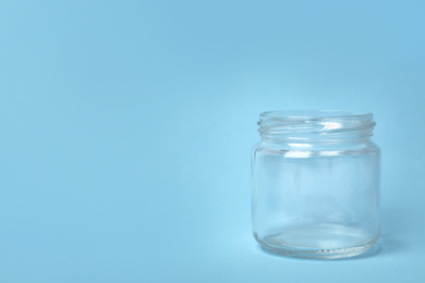 Open empty glass jar on light blue background, space for text