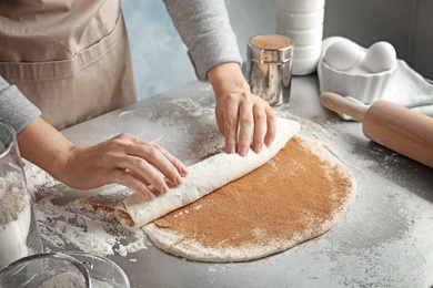 Photo of Woman making cinnamon rolls at table, closeup