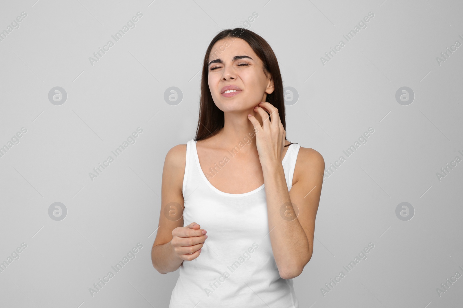 Photo of Young woman scratching neck on light background. Annoying itch
