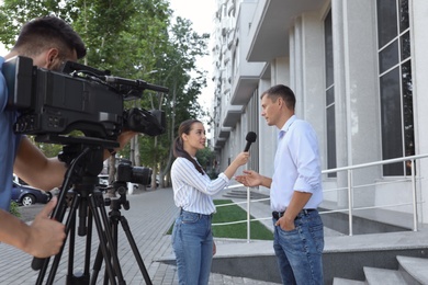 Photo of Professional journalist and operator with video camera taking interview outdoors
