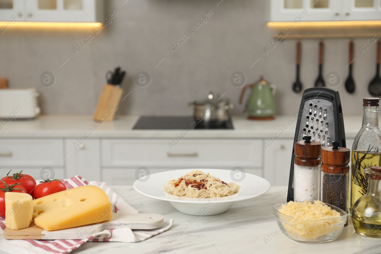 Photo of Delicious pasta with grated cheese and other products on white marble table in kitchen