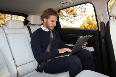 Young handsome man using laptop in back seat of car