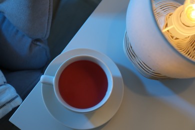 Cup of hot tea on white table at night, top view