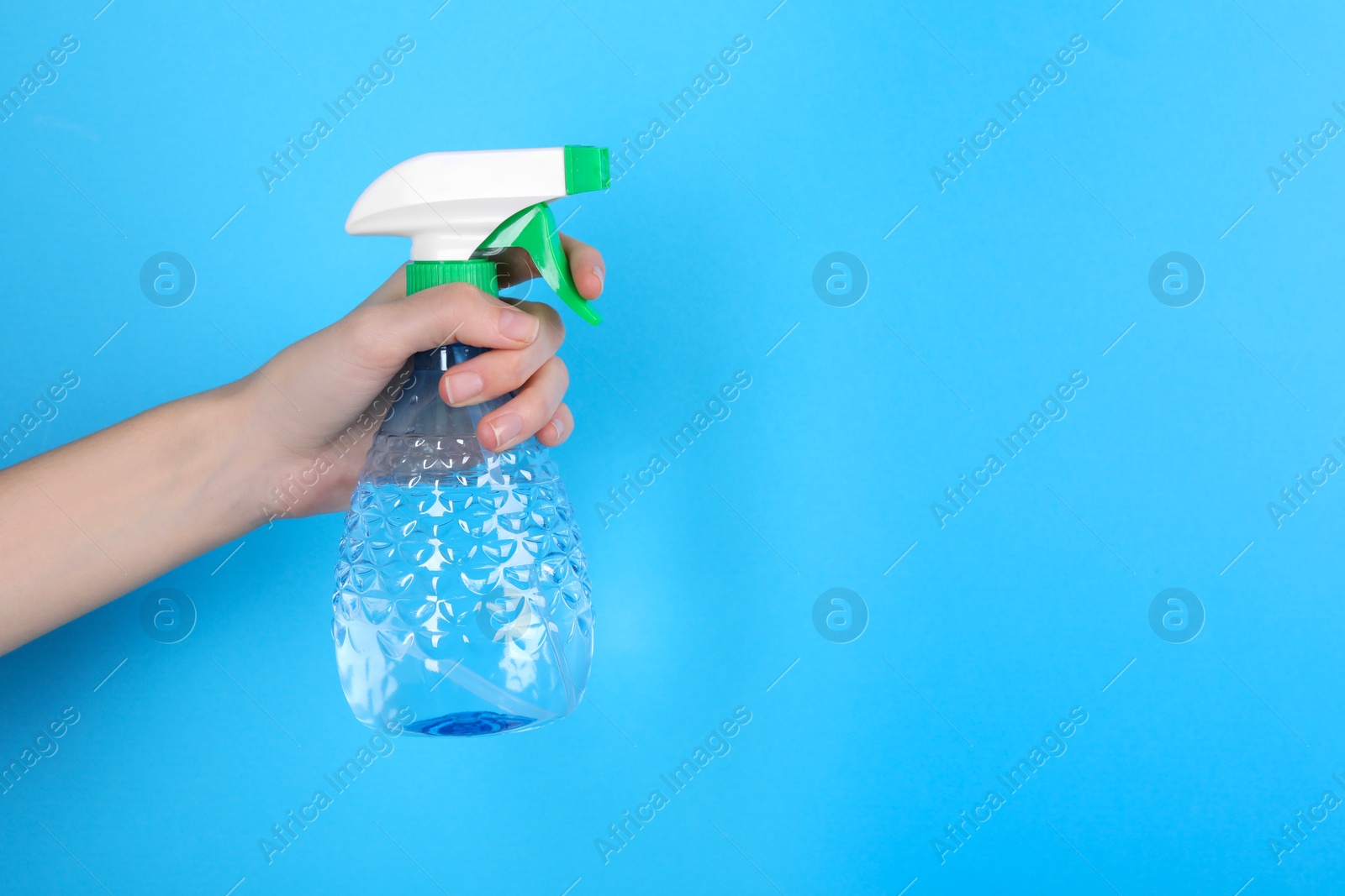 Photo of Woman holding plastic spray bottle on light blue background, closeup. Space for text