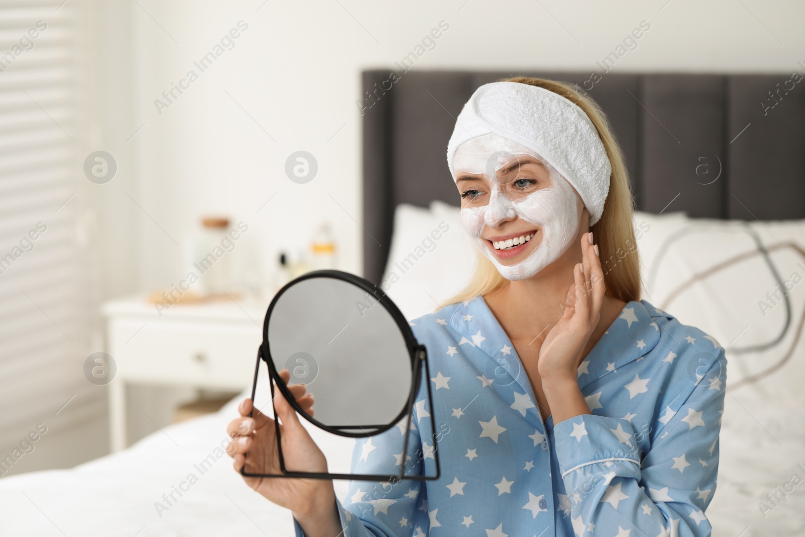 Photo of Young woman with face mask looking into mirror in bedroom. Spa treatments