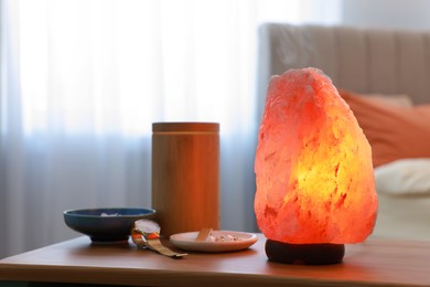 Photo of Himalayan salt lamp, air ionizer and accessories on wooden table in bedroom