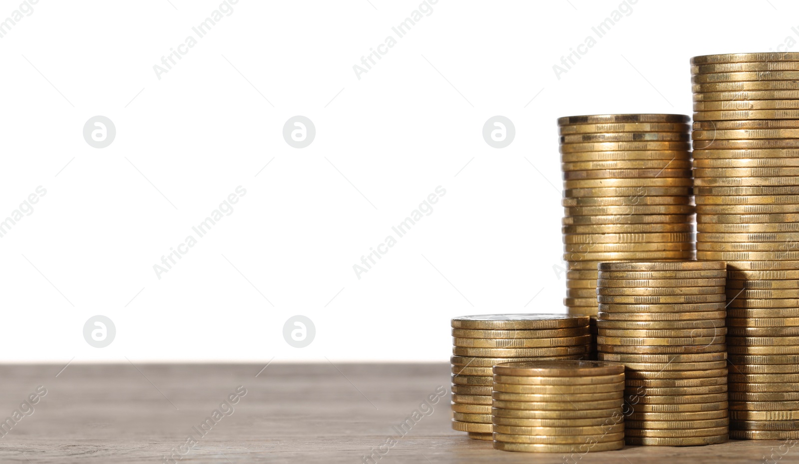 Photo of Many golden coins stacked on wooden table against white background, space for text