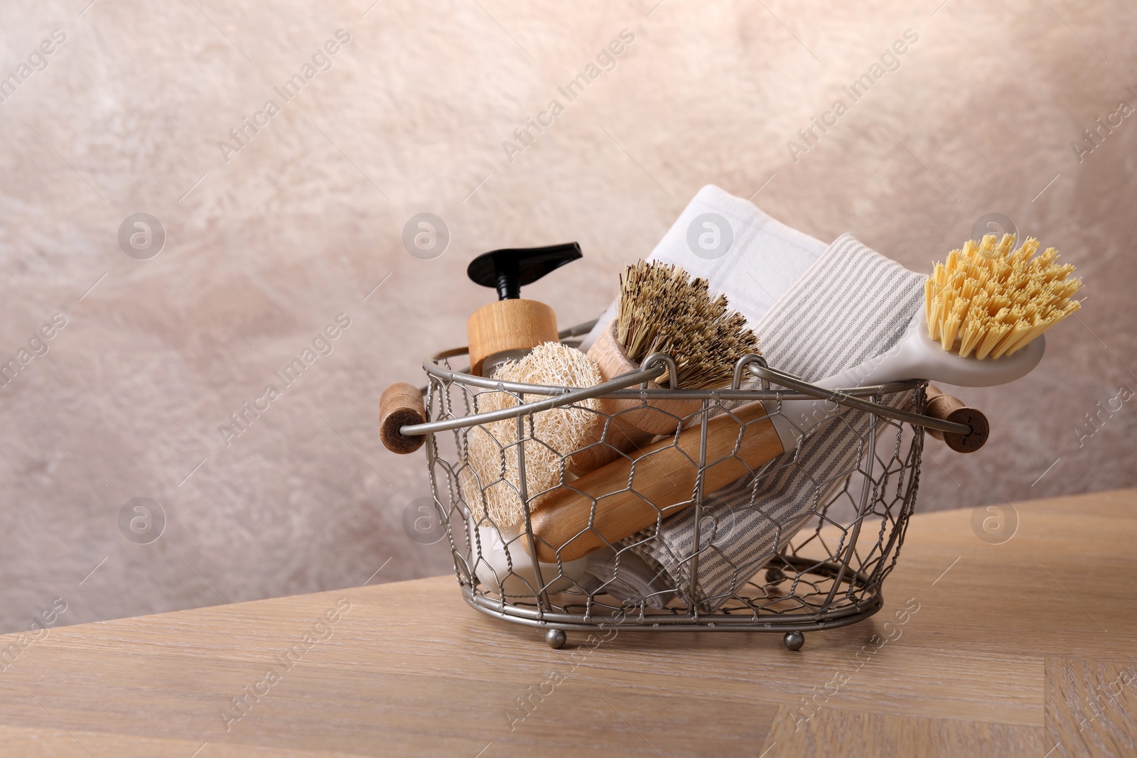 Photo of Metal basket with brushes and cleaning tools on wooden table. Space for text