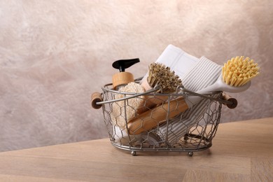 Metal basket with brushes and cleaning tools on wooden table. Space for text