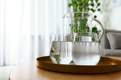 Tray with jug and glasses of water on wooden table in room, space for text. Refreshing drink