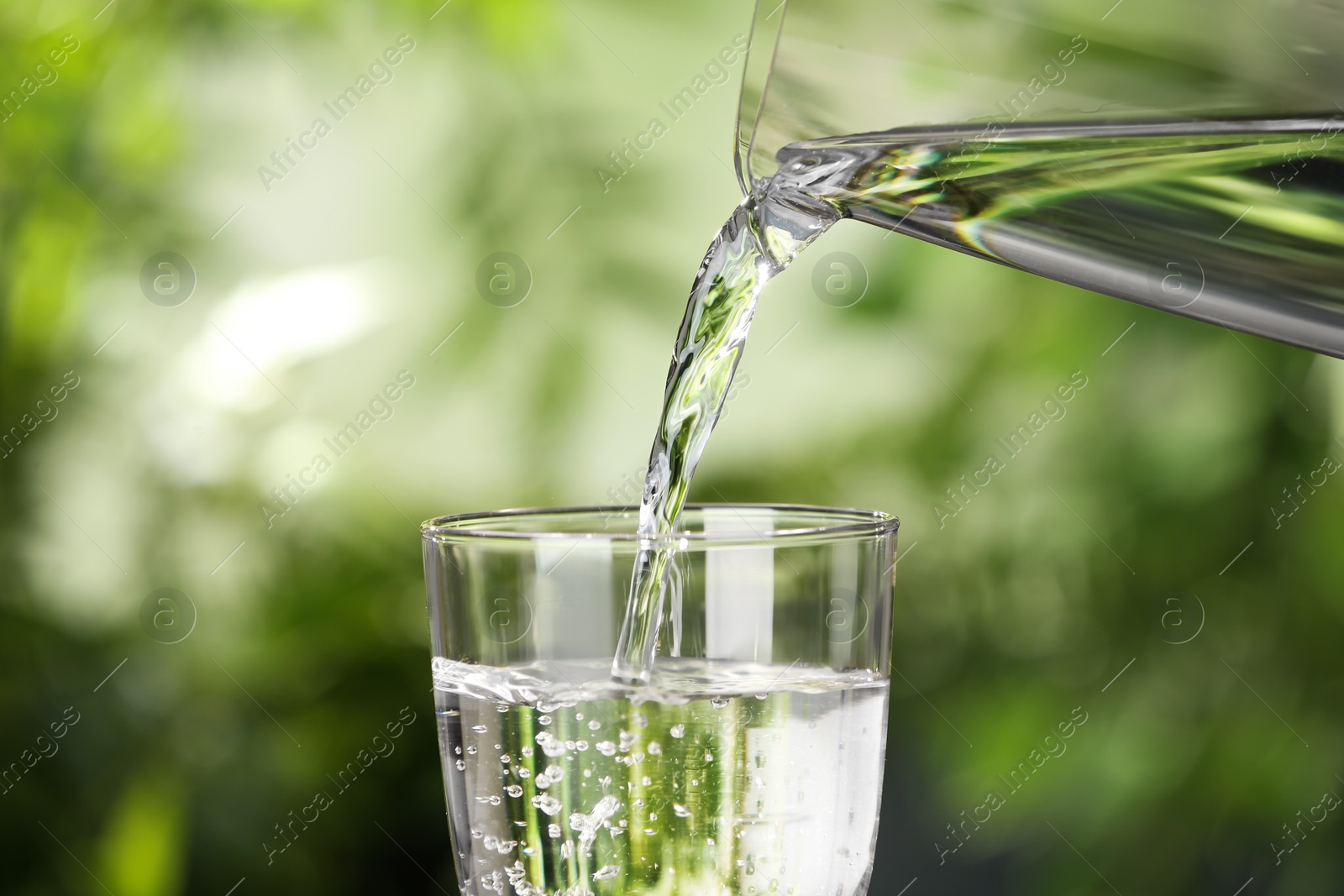 Photo of Pouring water from jug into glass on blurred background