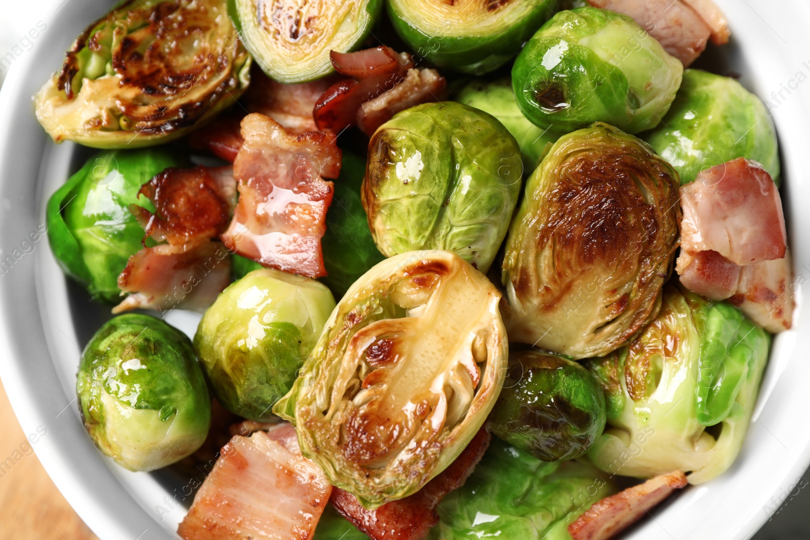 Photo of Delicious Brussels sprouts with bacon in bowl, closeup