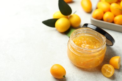 Delicious kumquat jam in jar and fresh fruits on white table, space for text