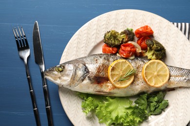 Photo of Delicious baked fish and vegetables served on blue wooden table, top view