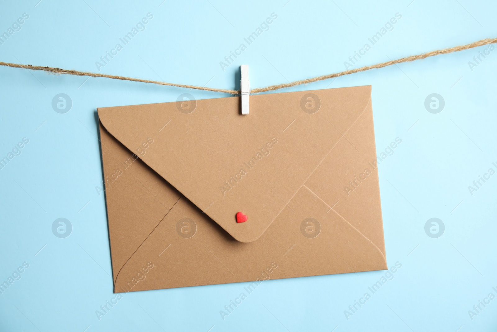 Photo of Envelope with small heart hanging on twine against light blue background. Love letter