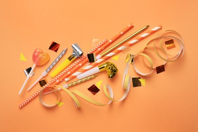 Party blowers, lollipop and festive decor on coral background, flat lay