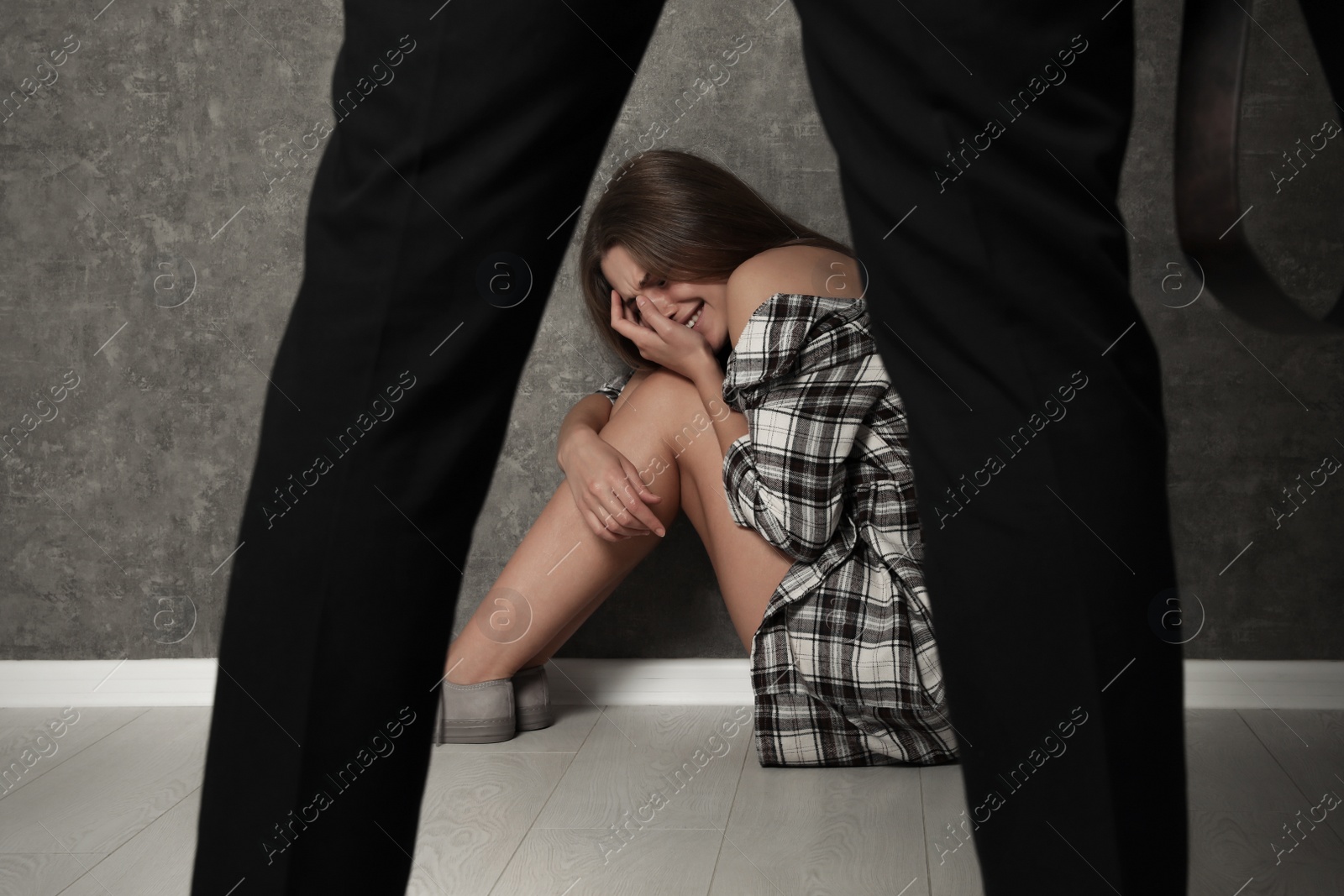 Photo of Man with belt standing in front of crying woman indoors. Stop sexual assault