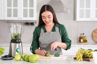 Young woman cutting broccoli for smoothie at white table in kitchen