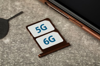 Photo of 6G and 5G technology, Internet concept. SIM cards in tray with smartphone on grey table, closeup