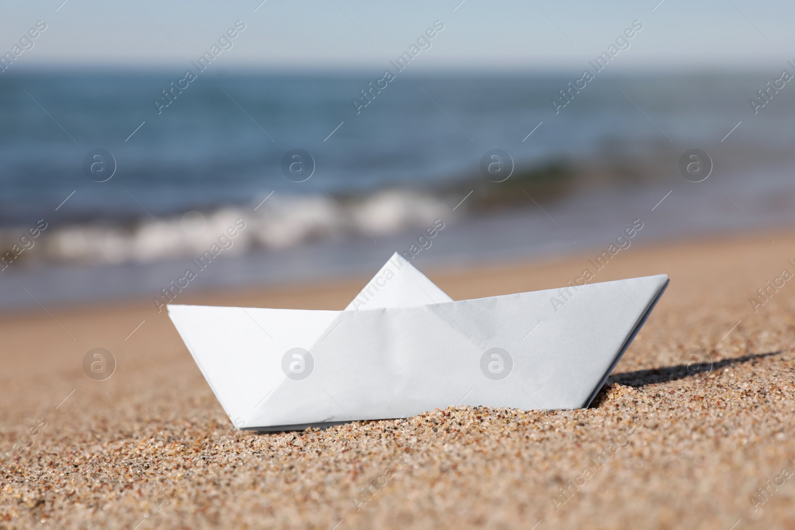 Photo of White paper boat near sea on sandy beach, closeup