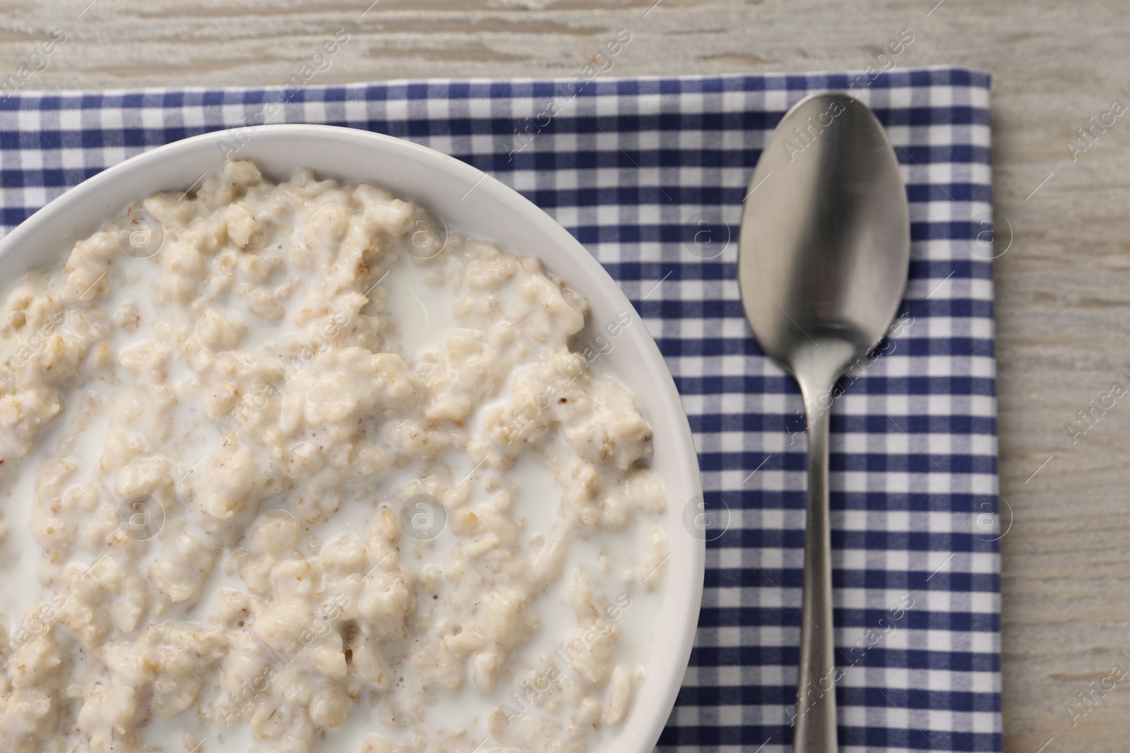 Photo of Tasty boiled oatmeal in bowl and spoon on wooden table, top view