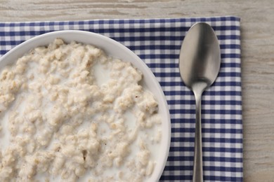 Tasty boiled oatmeal in bowl and spoon on wooden table, top view