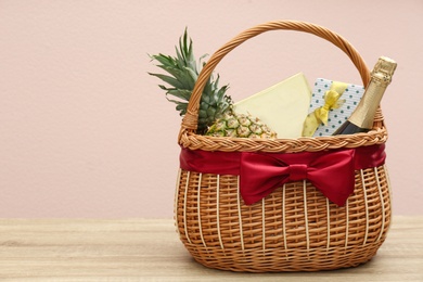 Wicker gift basket with pineapple and bottle of champagne on wooden table. Space for text