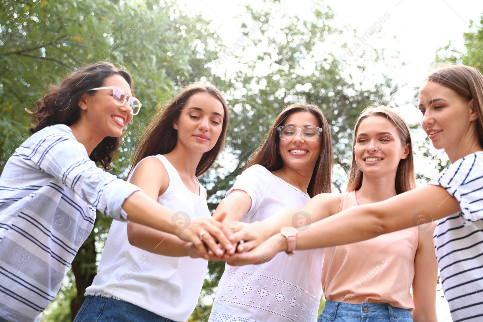 Photo of Happy women putting hands together outdoors on sunny day. Girl power concept