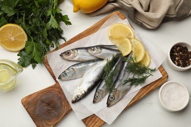 Photo of Fresh raw sprats, lemon and dill on white marble table, flat lay