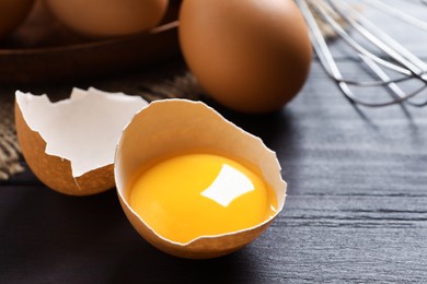 Photo of Cracked eggshell with raw yolk on dark wooden table