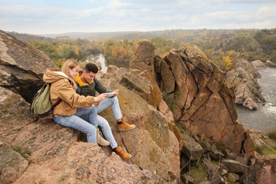 Couple of travelers with backpacks and map sitting on steep cliff. Autumn vacation