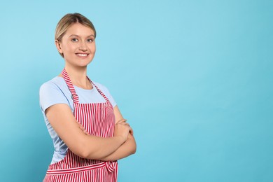 Beautiful young woman in clean striped apron on light blue background. Space for text
