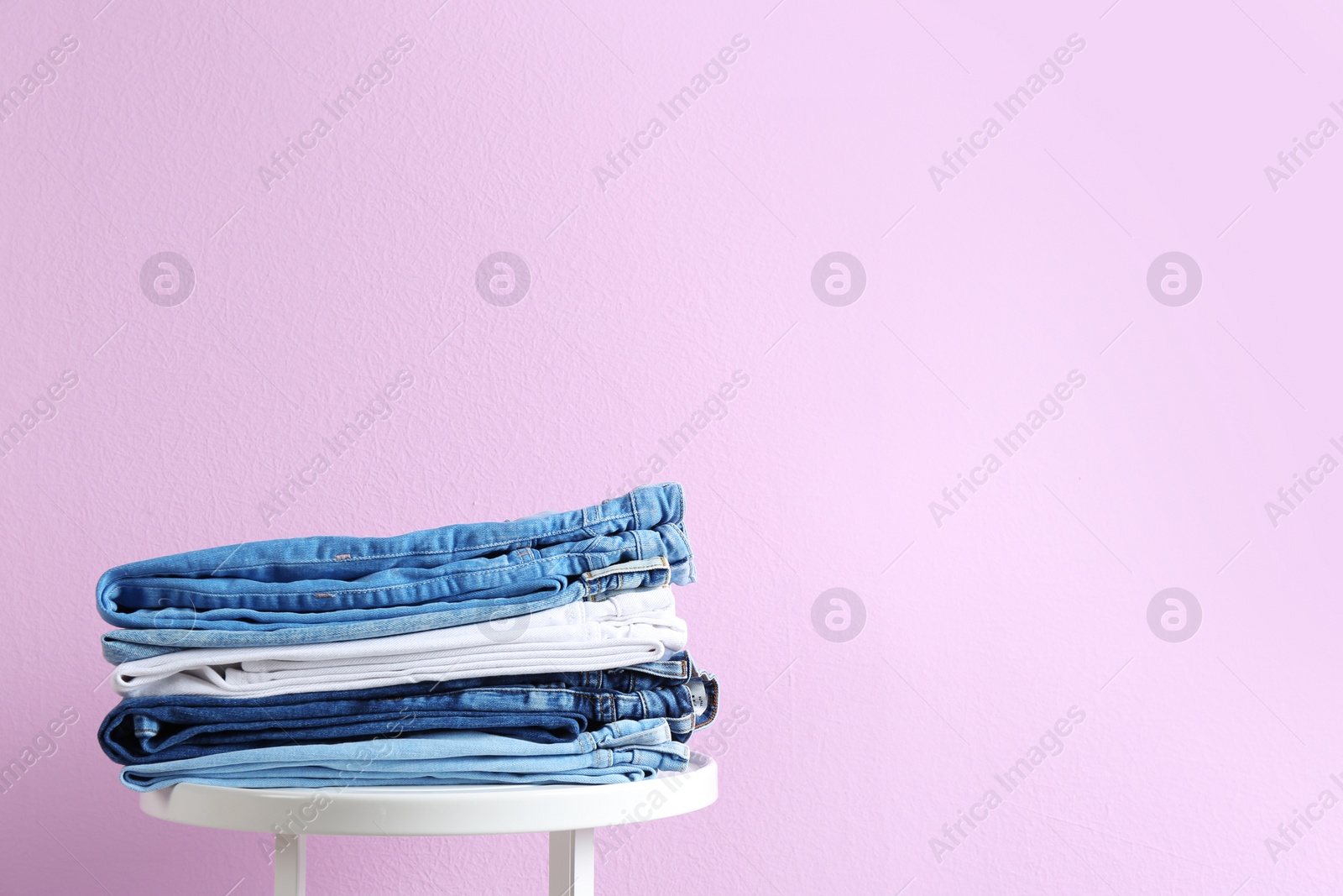 Photo of Stack of different jeans on table against color background