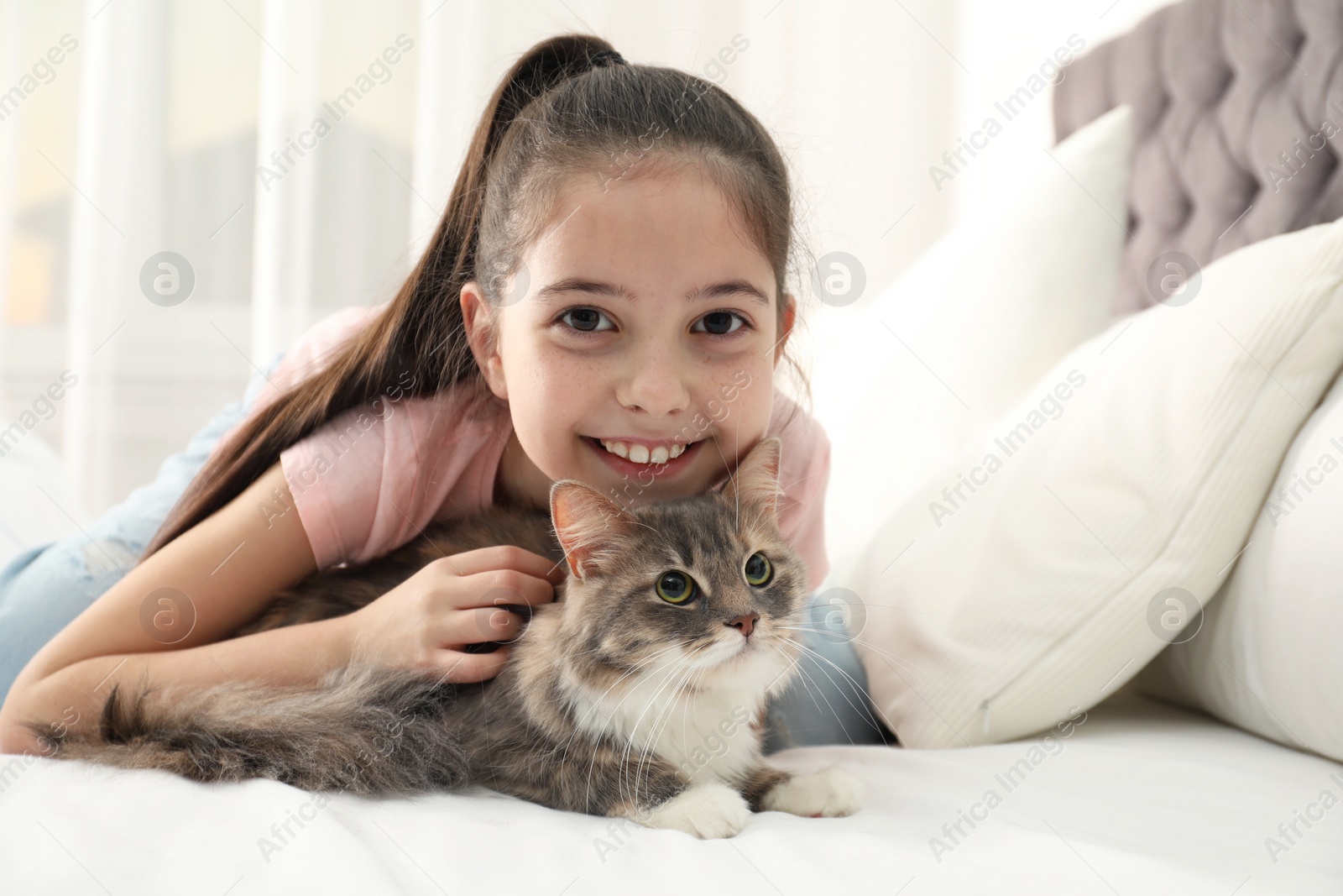 Photo of Cute little girl with cat lying on bed at home. First pet