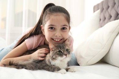 Cute little girl with cat lying on bed at home. First pet