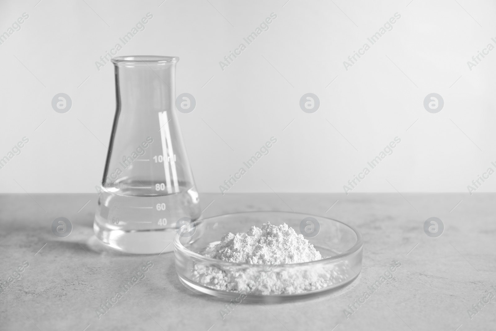 Photo of Petri dish with calcium carbonate powder and laboratory flask on light grey table. Space for text