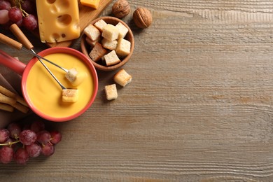 Pot of tasty cheese fondue and snacks on wooden table, flat lay. Space for text