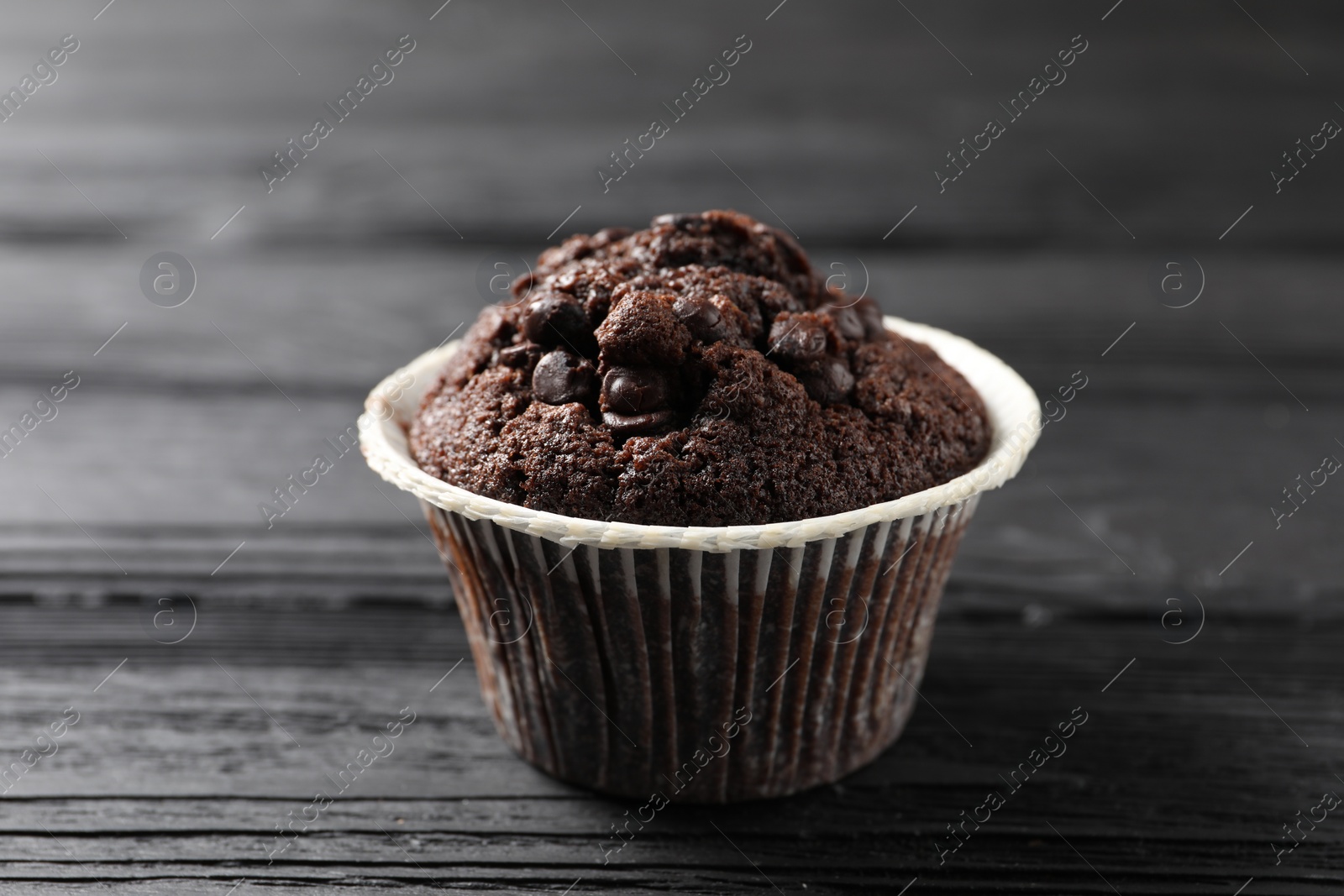 Photo of Delicious chocolate muffin on black wooden table, closeup