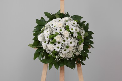 Photo of Funeral wreath of flowers on wooden stand against grey background