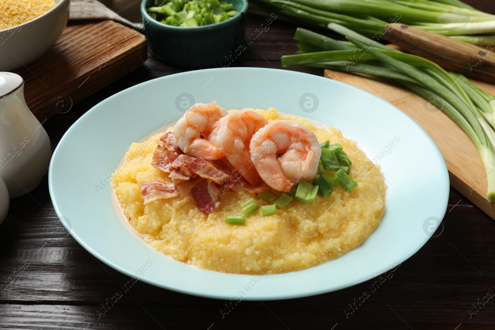 Photo of Plate with fresh tasty shrimps, bacon, grits and green onion on dark wooden table