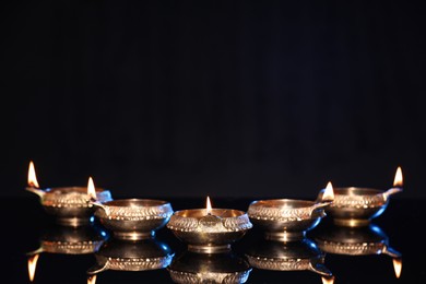 Photo of Many lit diyas on black background, space for text. Diwali lamps