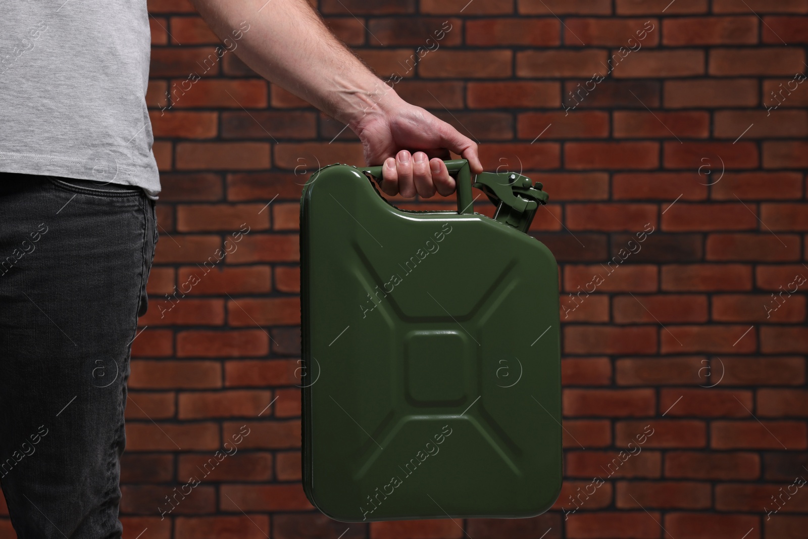 Photo of Man holding khaki metal canister against brick wall, closeup